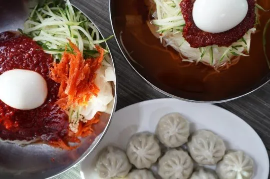 위에서 본 비빔밀면과 물밀면 두 그릇, 흰 접시의 만두