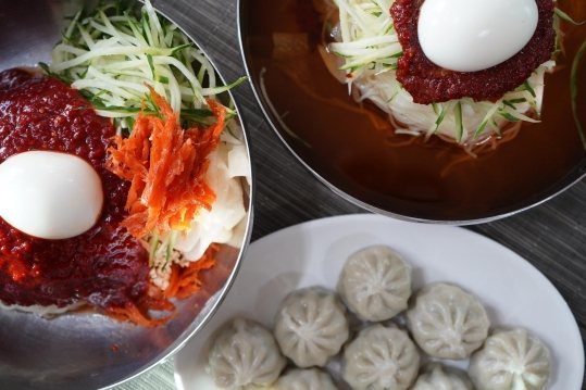 위에서 본 비빔밀면과 물밀면 두 그릇, 흰 접시의 만두
